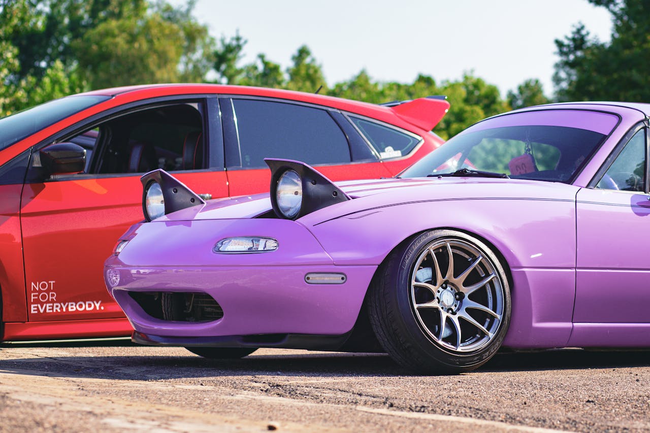 about-01 A vivid capture showcasing a customized purple and red car duo on a sunny day, perfect for auto enthusiasts.